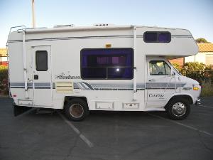 Side view of a white RV with a faded decal on a parking lot.