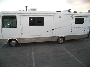 Side-view of a white RV with faded decals on a parking lot.