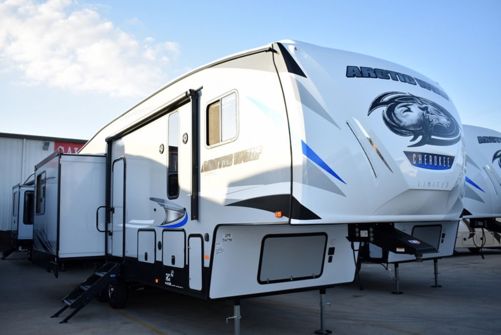 Two white & blue 2020 Forest River Arctic Wolf 298LB fifth wheel trailers parked in front of a …
