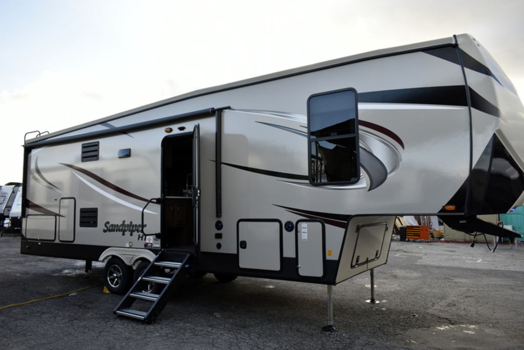White 2020 Forest River Sandpiper 39BARK 5th wheel trailer parked in front of other RVs and a …